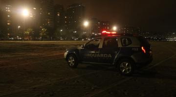 Viatura da GCM na praia e torres de iluminação acesas ao fundo #paratodosverem