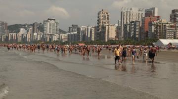 pessoas caminhando na praia à beira d'água. #paratodosverem 