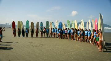Surfistas estão na areia da praia. Eles posam para foto cada um com sua prancha oca em pé. #Pracegover