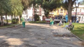 homens estão trabalhando em praça. Eles estão uniformizados. Há pedras de mosaico português em um canto. #paratodosverem