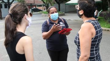 Agente da ouvidoria segura tablet enquanto conversa com duas mulheres em parque. #Paratodosverem