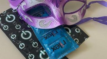 embalagens de preservativos sob uma máscara de carnaval. #paratodosverem 