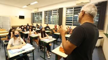 professor em primeiro plano e de costas para a foto. Alunos estão sentados assistindo a aula. #paratodosverem