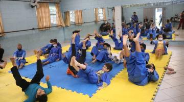 crianças vestidas com quimonos estão praticando judo sobre tatame. pelo movimento, elas parecem treinar queda no chão. #paratodosverem