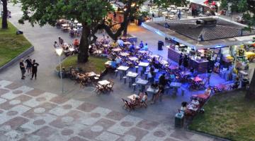 vista do alto, por drone, de quiosque no jardim da orla, com mesas em torno e público. #paratodosverem