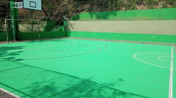 vista geral da quara, com pintura predominante verde, uma quadra de basquete e trave de gol ao fundo. #paratodosverem