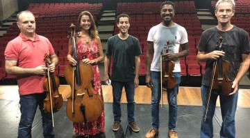 Cinco músicos segurando seus instrumentos sobre o palco. O do meio não segura. #paratodosverem