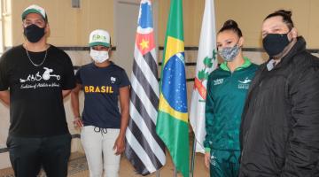 Eduardo Leonel e Vanessa Souza e Sarah Nascimento com sei treinador. Eles ladeiam as bandeiras de SP, Brasil e Santos. #paratodosverem