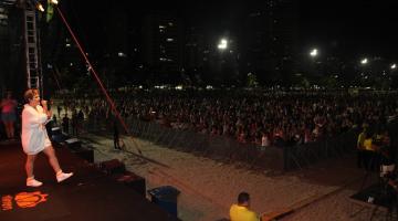 Cantora no palco e público ao fundo na Praia do Gonzaga. #pratodosverem