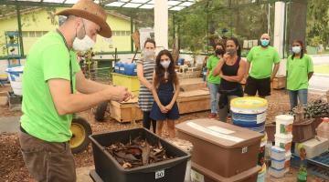 pessoa ensina técnica de compostagem e outras observam em centro #paratodosverem