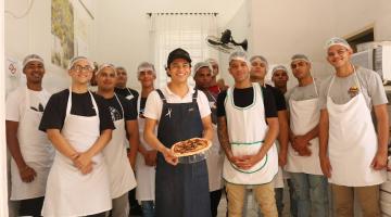 jovens estão reunidos para foto. O do meio segura uma pizza na forma. #paratodosverem 