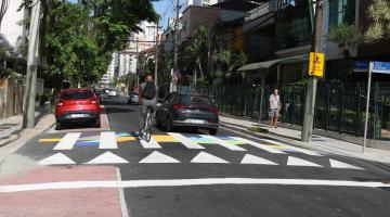 ciclista e carro passam sobre faixa de pedestre estilizada. #paratodosverem 