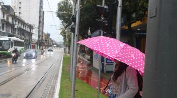 mulher de guarda-chuva espera para atravessar avenida. #paratodosverem