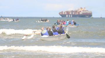 canoa havaiana no mar com diversos remadores empurrando 