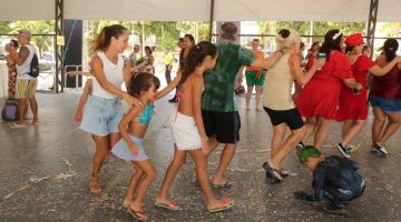 pessoas dançam sob tenda com confetes no chão. #paratodosverem