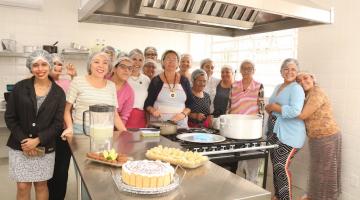 Grupo de mulheres à frente de mesa com doces e salgados. #paratodosverem
