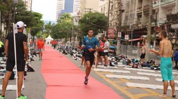 homem está correndo em rua sobre faixa vermelha. ao lado se vê grande estrutura esportiva, com bicicletas pelo chão.#paratodosverem 