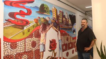 O artista junto com a pintura feita. #Paratodosverem.