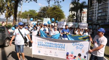 pessoas uniformizadas carregam faixa e cartazes na orla. #paratodosverem