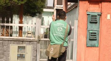 homem com colete de agente bate palma diante de casa. #paratodosverem