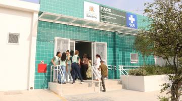 fachada de policlínica com pessoas na pequena escada de alvenaria que dá acesso ao prédio. #paratodosverem 