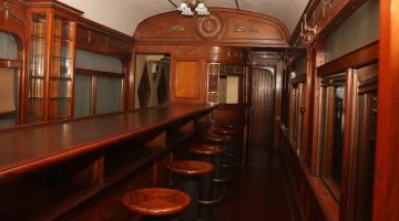 interior de carro ferroviário com balção de bar e bancos em madeira. #paratodosverem 