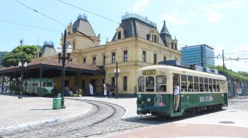 imagem mostra passagemd o bonde Japão com Estação do Valongo ao fundo #paratodosverem