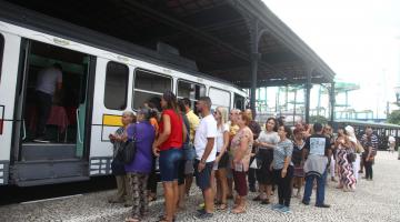 Pessoas fazem fila para ingressar no bonde arte. Ele está parado em estação. #Pracegover