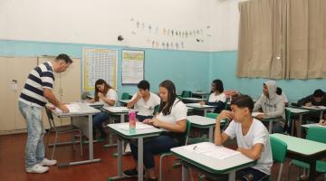 professor está em pé em sala diante de alunos sentados. #paratodoverem 