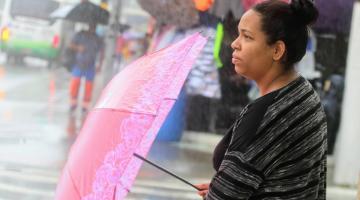mulher segurando guarda chuva olha para frente em dia chuvoso #paratodosverem