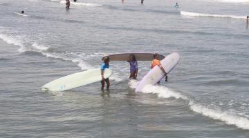 mulheres entram no mar com pranchões. #dparatodosverem