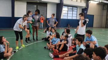 tecnica e atletas conversam com alunos sentados em quadra #paratodosverem