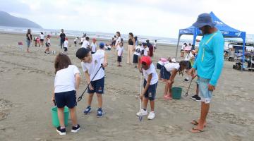 alunos uniformizados recolhem resíduos da areia da praia. #paratodosverem