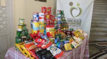 em uma mesa sacos de arroz, pacotes de feijão, latas de diversos produtos #paratodosverem