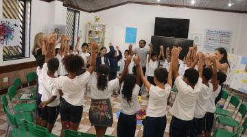 alunos estão de mãos dadas para o alto, reunidos em roda. #paratodosverem 