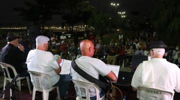 artistas tocando em palco e publico acompanhando sentado em praça #paratodosverem