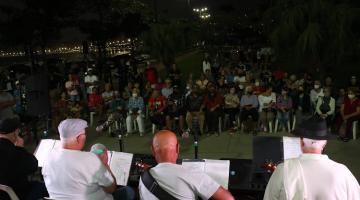musicos tocam e plateia assiste sentada a noite em praça #paratodosverem