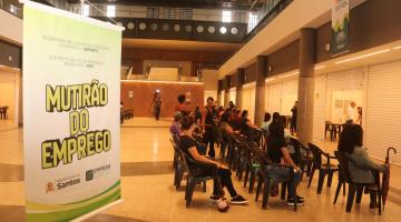 banner sobre mutirão com pessoas sentadas ao fundo. #paratodosverem