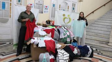 duas pessoas seguram roupas ao lado das doações #paratodosverem
