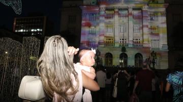 mulher com bebê assiste a projeção mapeada #paratodosverem