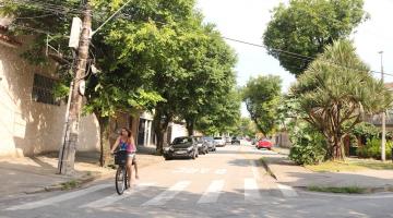 vista geral de rua arborizada. À frente e à esquerda, uma mulher está dirigindo uma bicicleta. #paratodosverem