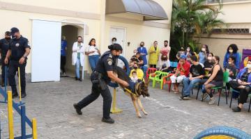 guarda conduz cachorro que pula enquanto pessoas observam #paratodosverem