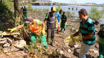 homens estão recolhendo detritos em área de mangue. Todos usam luvas. #paratodosverem 