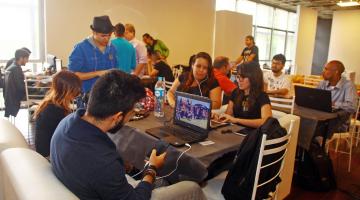 Jovens estão sentados em sofás, diante de mesas e na frente de seus notebooks. #Pracegover