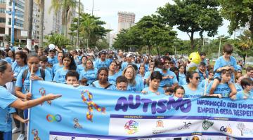 centenas de pessoas caminham na orla da praia segurando uma faixa