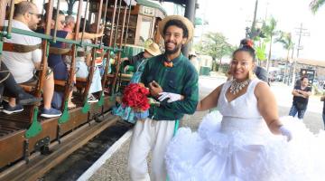 casal de noivos caipira sorri para foto e interage com passageiros sentados nos bancos do bonde. #paratodosverem