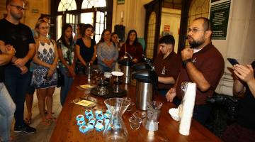 pessoa fala com mesa com café e doces para outras pessoas #paratodosverem