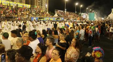 passarela do samba lotada de público com escola passando ao fundo. #paratodosverem 