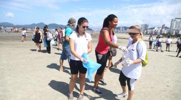 Mulheres recolhem lixo com sacolas na praia #pracegover 