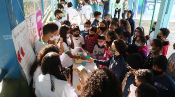 crianças cercam mesa com outros estudantes mostrando objetos #paratodosverem